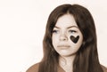 Portrait of a sad, sweet girl with blue eyes and a black paper heart pasted on her cheek close-up. unrequited love. Royalty Free Stock Photo