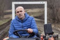 Portrait of sad tired man driving a tractor without cab during rain. Wet dirt road in the background. Royalty Free Stock Photo