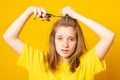 Portrait of sad and unhappy teen girl cutting her hair with scissors while standing over yellow background. Royalty Free Stock Photo