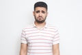 Portrait of sad updet or bored bearded young man in striped t-shirt standing and looking at camera with dissatisfied sadness face Royalty Free Stock Photo