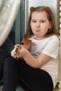 Portrait of sad upset little girl in white t-shirt and black leggings sitting inside of home and playing ukulele.