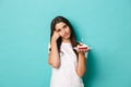 Portrait of sad woman having birthday, looking upset and gloomy, holding bday cake with lit candle, standing over blue