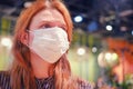 Portrait of a sad woman in a medical mask at a table in a cafe. The face of a girl with influenza coronavirus in a restaurant