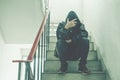 Portrait of sad young man covering his face with hands sitting on old stairs.