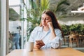 Portrait of sad young redhead woman in a coffee shop looking at smart phone. A lonely unhappy 30s girl siting in a cafe Royalty Free Stock Photo