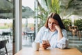 Portrait of sad young redhead woman in a coffee shop looking at smart phone. A lonely unhappy 30s girl siting in a cafe Royalty Free Stock Photo