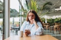 Portrait of sad young redhead woman in a coffee shop looking at smart phone. A lonely unhappy 30s girl siting in a cafe Royalty Free Stock Photo