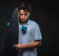 Portrait of a sad young skater boy dressed in a white t-shirt holds a longboard. on the dark background. Royalty Free Stock Photo