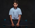 Portrait of a sad young skater boy dressed in a white t-shirt holds a longboard. on the dark background. Royalty Free Stock Photo