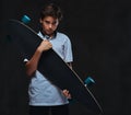 Portrait of a sad young skater boy dressed in a white t-shirt holds a longboard. on the dark background. Royalty Free Stock Photo