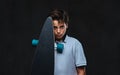 Portrait of a sad young skater boy dressed in a white t-shirt holds a longboard. Isolated on the dark background. Royalty Free Stock Photo