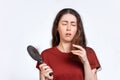 Portrait of a saddened brunette woman holds a comb with hair falling out and looks at the tips of her hair.White background