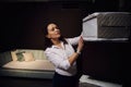 Portrait of a saleswoman working in a furniture store, putting orthopedic mattress samples on the stand, standing against