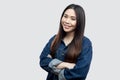 Portrait of satisfied beautiful brunette asian young woman in casual blue jacket with makeup standing, crossed arms, toothy Royalty Free Stock Photo