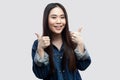 Portrait of satisfied beautiful brunette asian young woman in casual blue jacket with makeup standing, thumbs up, toothy smiling Royalty Free Stock Photo