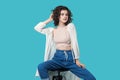 Portrait of satisfied beautiful young brunette woman in casual style sitting on chair and posing like fashion model and looking at Royalty Free Stock Photo