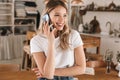 Portrait of satisfied blond woman talking on cell phone while standing in stylish wooden kitchen at home Royalty Free Stock Photo