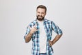 Portrait of satisfied and confident looking bearded man, holding one hand on waist and making rock gesture with another