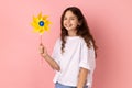 Delighted charming little girl holding paper windmill, playing with pinwheel toy on stick. Royalty Free Stock Photo