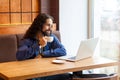 Portrait of satisfied handsome intelligence young adult man freelancer in casual style sitting in cafe with laptop, drinking cup Royalty Free Stock Photo