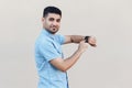 Portrait of satisfied handsome young bearded man in blue shirt standing, pointing and holding his smart watch, looking at camera Royalty Free Stock Photo