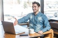 Portrait of satisfied happy young businessman in blue jeans shirt are sitting in cafe and greeting a worker through a webcam and Royalty Free Stock Photo