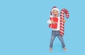 Portrait of a satisfied little child boy in christmas Santa hat. laughing isolated over blue background. Holds a gift box and big Royalty Free Stock Photo