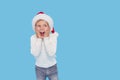 Portrait of a satisfied little child boy dressed in christmas Santa hat. laughing isolated over blue background. Wow face. Royalty Free Stock Photo