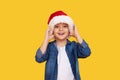 Portrait of a satisfied little child boy dressed in christmas Santa hat. laughing isolated over colored yellow background. Royalty Free Stock Photo