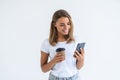 Portrait of a satisfied young woman using mobile phone while holding cup of coffee to go isolated over white background Royalty Free Stock Photo