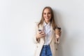 Portrait of a satisfied young businesswoman using mobile phone while holding cup of coffee to go over white background Royalty Free Stock Photo