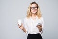 Portrait of a satisfied young business woman using mobile phone while holding cup of coffee to go over white background Royalty Free Stock Photo