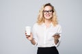 Portrait of a satisfied young business woman using mobile phone while holding cup of coffee to go over white background Royalty Free Stock Photo