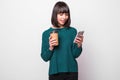 Portrait of a satisfied young woman in green sweater using mobile phone while holding cup of coffee to go isolated over white Royalty Free Stock Photo