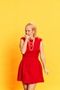 Portrait of scared blond woman in retro clothes biting fist with frightening face on yellow background. Fear, problem