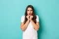 Portrait of scared and frustrated brunette female model in white t-shirt, frowning and looking alarmed, standing over