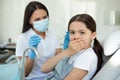 Portrait of scared girl covering mouth with hands with dentist holding instruments