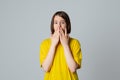 Portrait of a scared teen girl in yellow casual t shirt, looking at camera with wide opened eyes, covering mouth her hands, stand Royalty Free Stock Photo