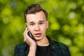 Portrait of scared White young guy writes a message on the mobile phone and smiles. Man on green bokeh background