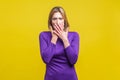 Portrait of scared young woman covering her mouth with hands. indoor studio shot isolated on yellow background