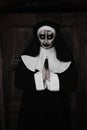 Portrait of scary devilish nun with clasped hands near wooden door outdoors. Halloween party look Royalty Free Stock Photo