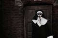 Portrait of scary devilish nun near red brick wall, space for text. Halloween party look