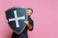 Portrait of scary man, medieval warrior or archer in armor hiding himself behind a shield isolated over pink studio Royalty Free Stock Photo