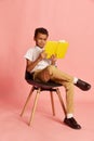 Portrait of school age american-african boy, pupil in uniform reading book over pink background. Concept of new Royalty Free Stock Photo