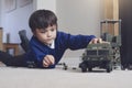 Portrait of School boy lying down on the carpet floor playing with soldiers, military car and figurine toys, Happy Kid playing