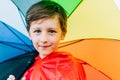 Portrait of a school boy with rainbow umbrella behind. Kid holds colourful umbrella on his shoulder. Cheerful child in a Royalty Free Stock Photo