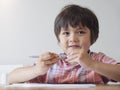 Portrait of school kid boy siting on table doing homework, Happy Child holding grey colour paint,A boy drawing blue colour on