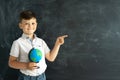 portrait of a schoolboy at school with a globe standing in front of a chalk board and pointing his finger to the right Royalty Free Stock Photo