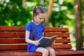 Portrait of schoolgirl on a bench reading book. Background city park. Royalty Free Stock Photo