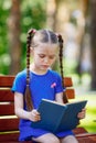 Portrait of schoolgirl on a bench reading book. Background city park. Royalty Free Stock Photo